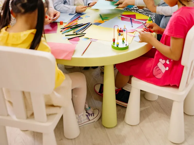 Preschool teachers and children doing a paper craft activity together at a table